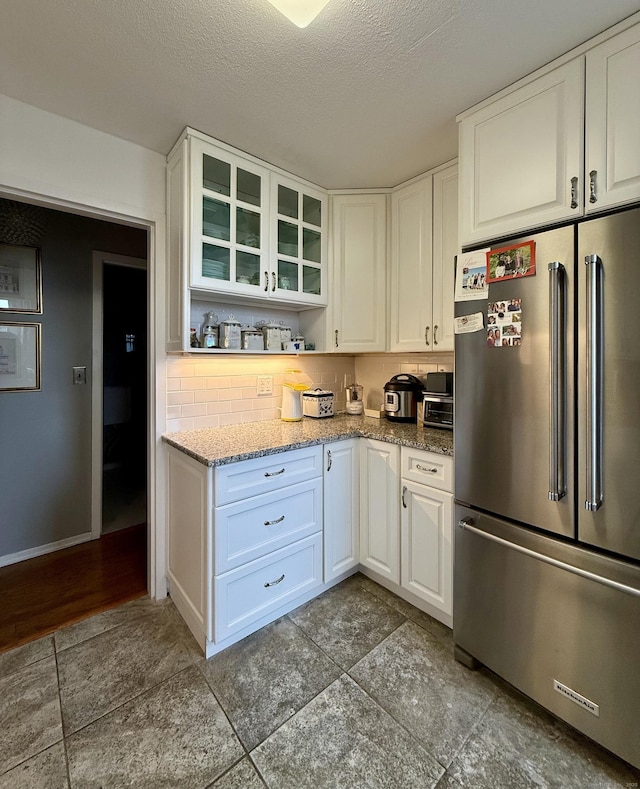 1 Strawberry Hill Ct Apt 6F, Stamford, CT 06902 - kitchen with high end fridge, white cabinetry, tasteful backsplash, glass insert cabinets, and a textured ceiling
