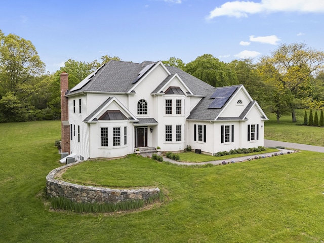 24 N Racebrook Rd, Woodbridge, CT 06525 - view of front of home with solar panels, a chimney, roof with shingles, a front yard, and stucco siding