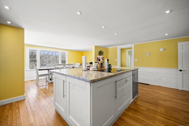 kitchen featuring black electric cooktop, a center island, light wood-style flooring, wainscoting, and light stone countertops