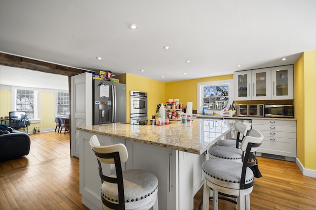 kitchen featuring appliances with stainless steel finishes, light wood-style flooring, light stone counters, glass insert cabinets, and recessed lighting