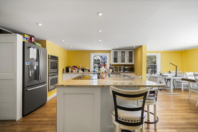 kitchen featuring stainless steel appliances, light wood finished floors, light stone countertops, glass insert cabinets, and white cabinetry