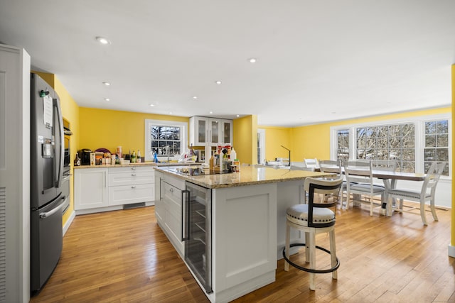 kitchen featuring beverage cooler, stainless steel appliances, a kitchen island, a breakfast bar area, and white cabinetry