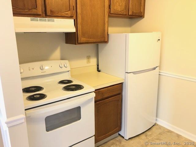 452 Judd Sq Unit 452, Wallingford, CT 06492 - kitchen with white appliances, under cabinet range hood, light countertops, brown cabinetry, and baseboards