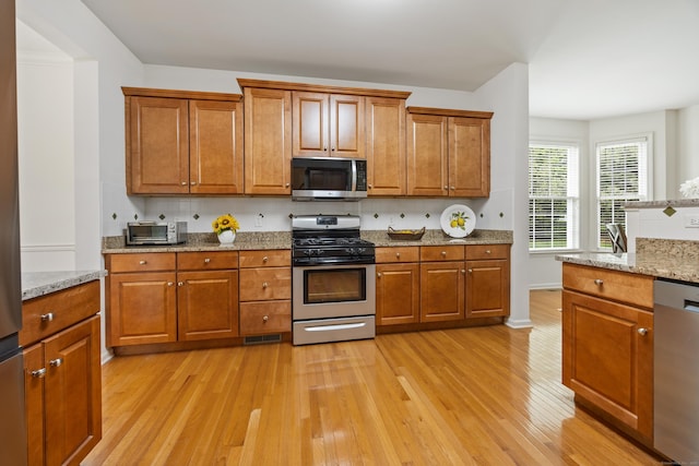 1 Chatham Ct Unit 1, Middlebury, CT 06762 - kitchen featuring appliances with stainless steel finishes, light wood-style flooring, brown cabinets, and light stone counters