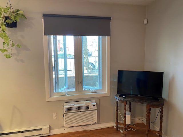 detailed view of baseboard heating, a wall unit AC, wood finished floors, and baseboards