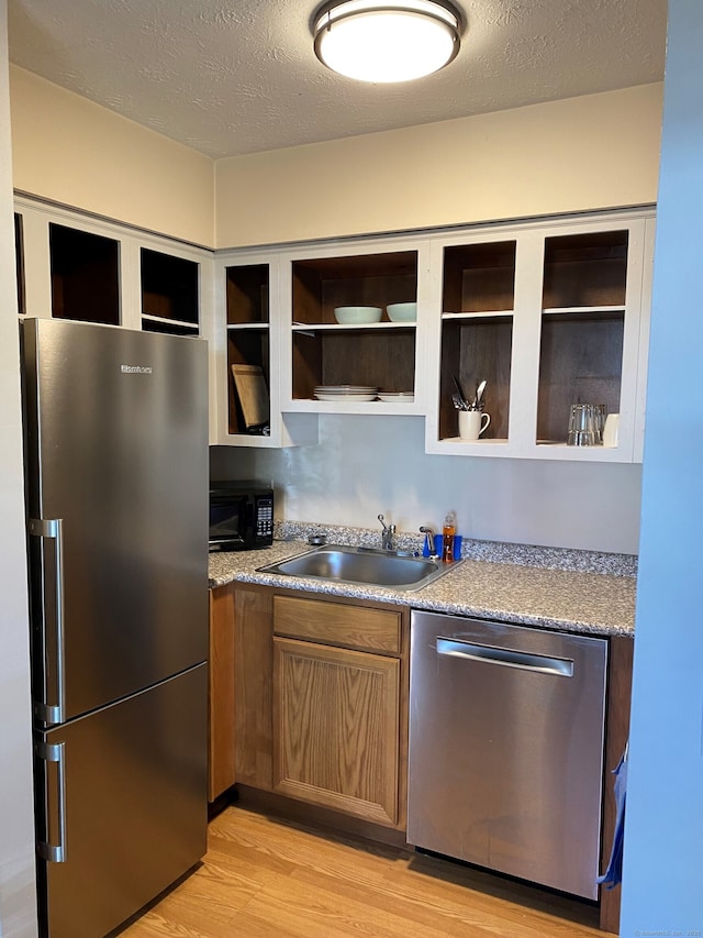 kitchen featuring stainless steel appliances, a sink, light wood-style floors, a textured ceiling, and open shelves