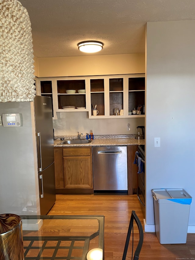 kitchen with stainless steel appliances, a sink, open shelves, light wood-style flooring, and light stone countertops