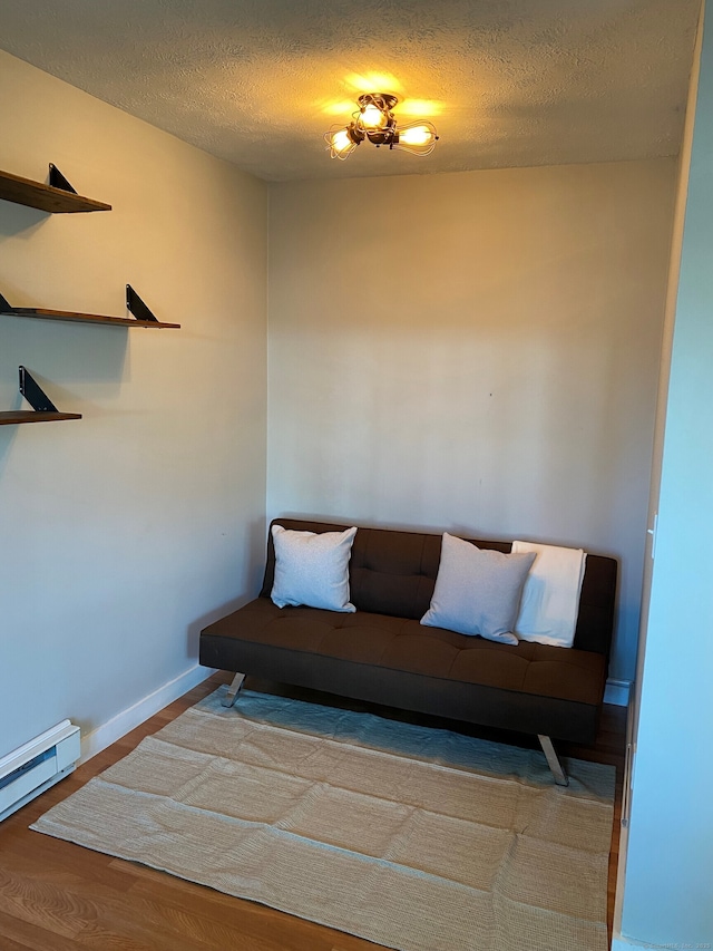 living area with baseboard heating, wood finished floors, a textured ceiling, and baseboards