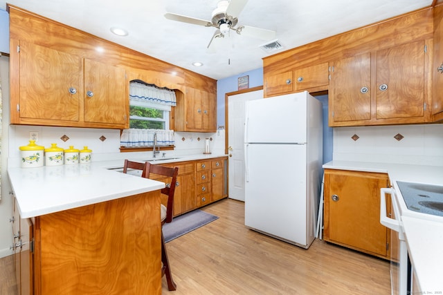 kitchen featuring white appliances, brown cabinetry, a sink, light wood-style flooring, and recessed lighting