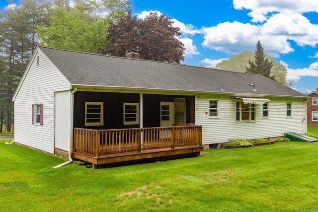 rear view of property featuring a lawn, a shingled roof, a chimney, and a deck