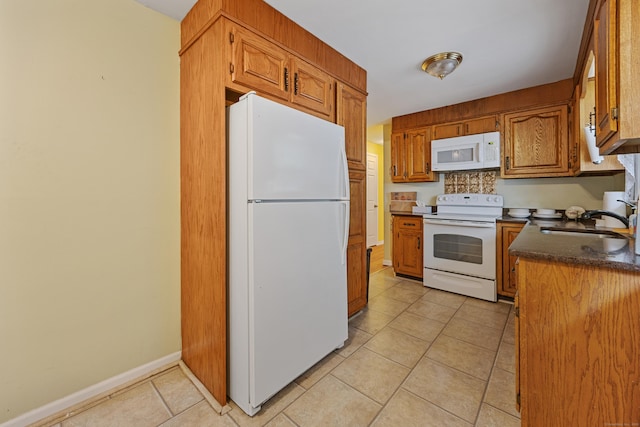 kitchen featuring white appliances, a sink, light tile patterned flooring, dark countertops, and brown cabinets