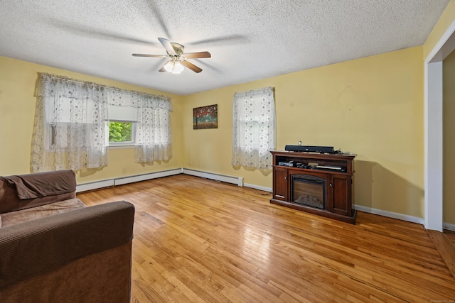living area with a baseboard radiator, ceiling fan, light wood-style flooring, a fireplace, and a textured ceiling