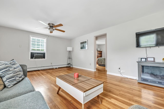 living area with a baseboard heating unit, ceiling fan, light wood-type flooring, cooling unit, and baseboards