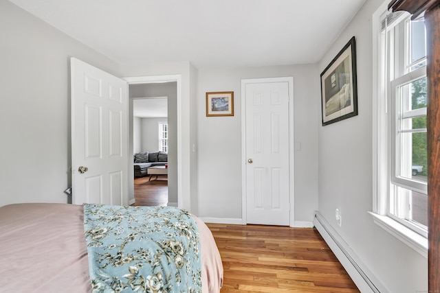 bedroom with a baseboard heating unit, light wood-style floors, and baseboards