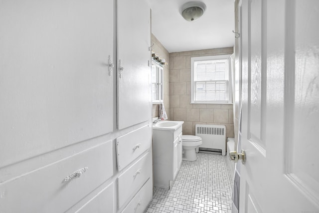 full bath with radiator heating unit, toilet, tile patterned floors, vanity, and tile walls