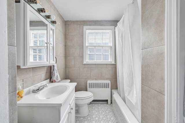 full bath with radiator heating unit, tile walls, vanity, toilet, and shower / bath combo