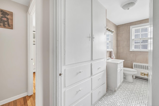bathroom with radiator heating unit, tile walls, toilet, vanity, and tile patterned floors