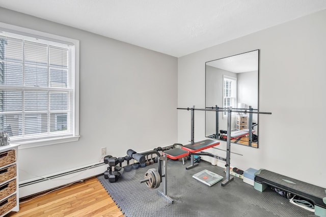 exercise room with baseboard heating, wood finished floors, and baseboards