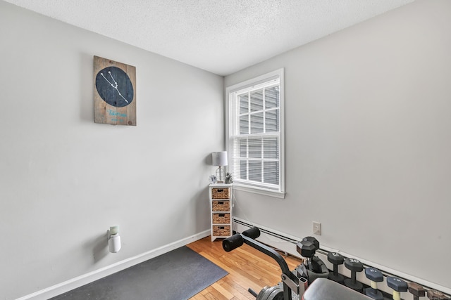 workout area with wood finished floors, a textured ceiling, and baseboards