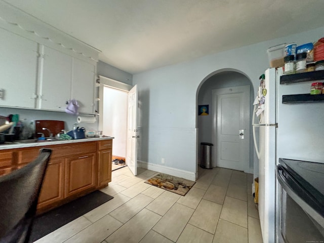 kitchen featuring arched walkways, electric range oven, light countertops, brown cabinets, and baseboards