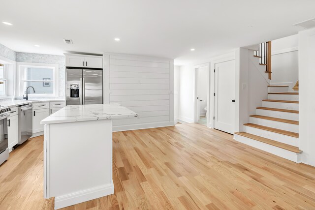 119 Melba St, Milford, CT 06460 - kitchen with appliances with stainless steel finishes, a center island, a sink, light wood finished floors, and white cabinetry