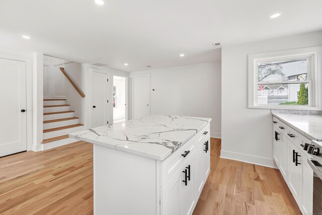 119 Melba St, Milford, CT 06460 - kitchen featuring light wood-type flooring, a kitchen island, light stone countertops, stove, and white cabinets