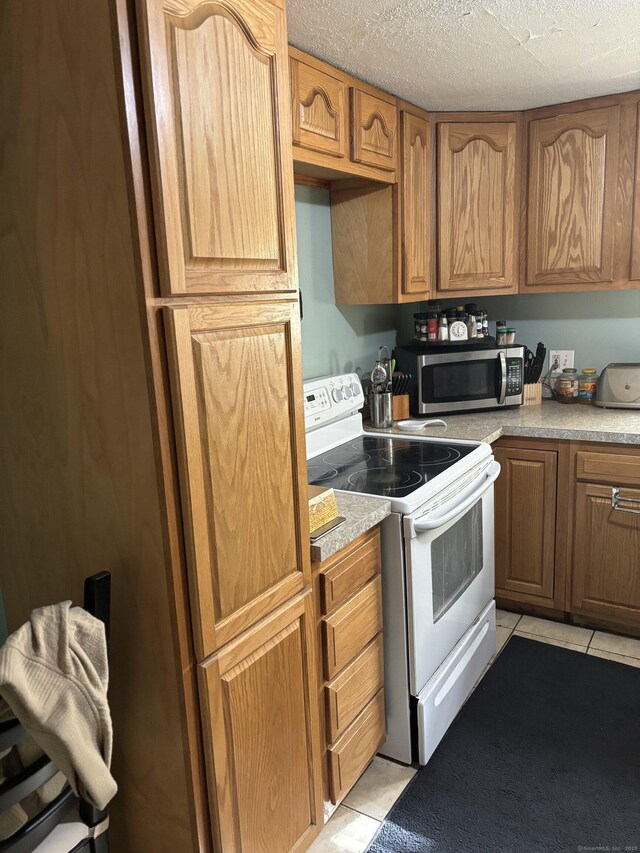 6 Peach St, Waterbury, CT 06708 - kitchen featuring stainless steel microwave, electric range, light tile patterned flooring, light countertops, and brown cabinetry