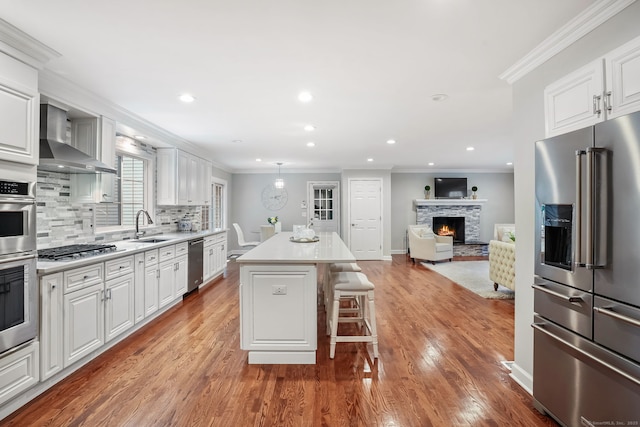 22 Fox Run, Wilton, CT 06897 - kitchen with stainless steel appliances, wall chimney range hood, a stone fireplace, light wood-style floors, and a sink