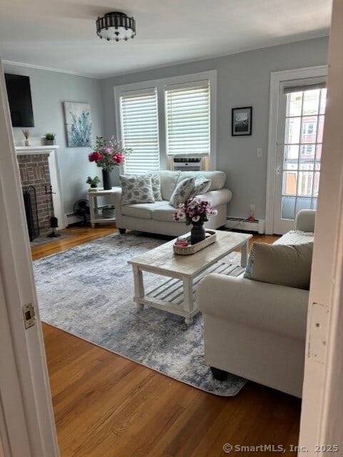 living area featuring plenty of natural light, baseboard heating, wood finished floors, and a fireplace
