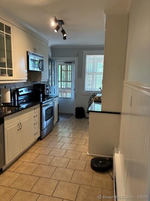 kitchen with appliances with stainless steel finishes, dark countertops, wainscoting, glass insert cabinets, and a sink