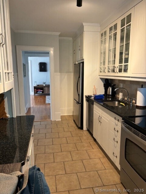 kitchen with stainless steel appliances, a sink, white cabinetry, glass insert cabinets, and dark stone counters