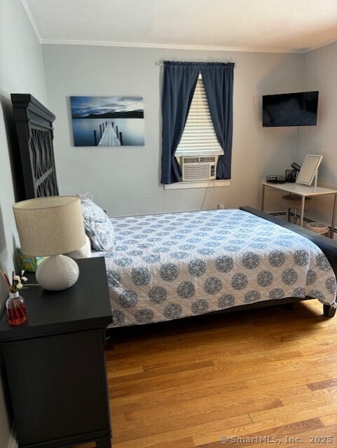 bedroom featuring wood finished floors, ornamental molding, and cooling unit