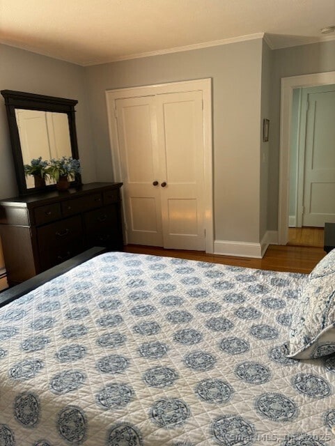 bedroom with wood finished floors, crown molding, baseboards, and a closet