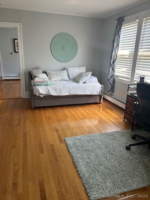 bedroom with a baseboard heating unit, ornamental molding, hardwood / wood-style floors, an office area, and a baseboard radiator
