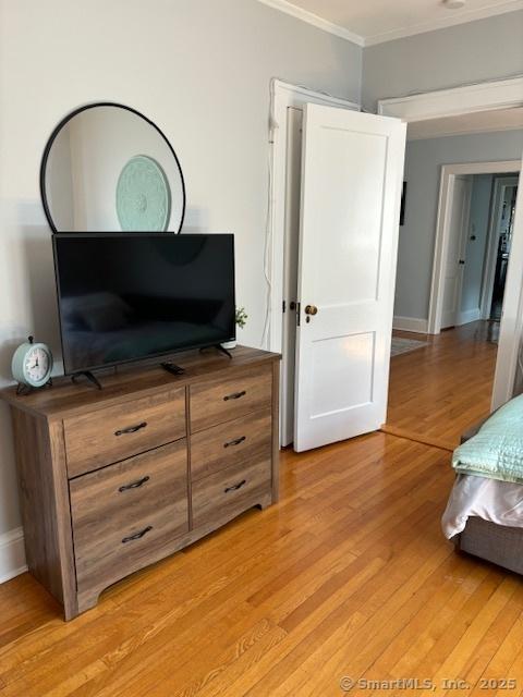bedroom with ornamental molding, light wood-style flooring, and baseboards