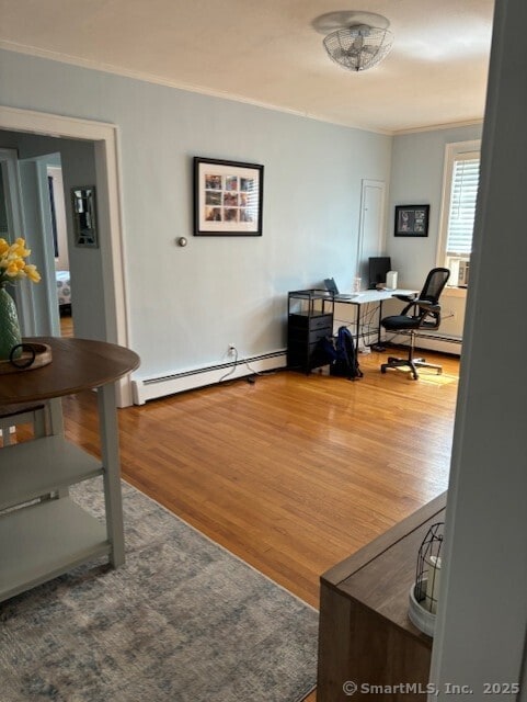 office space featuring a baseboard heating unit, ornamental molding, and wood finished floors