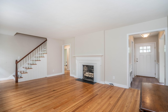 unfurnished living room with stairway, light wood finished floors, a fireplace with flush hearth, and baseboards