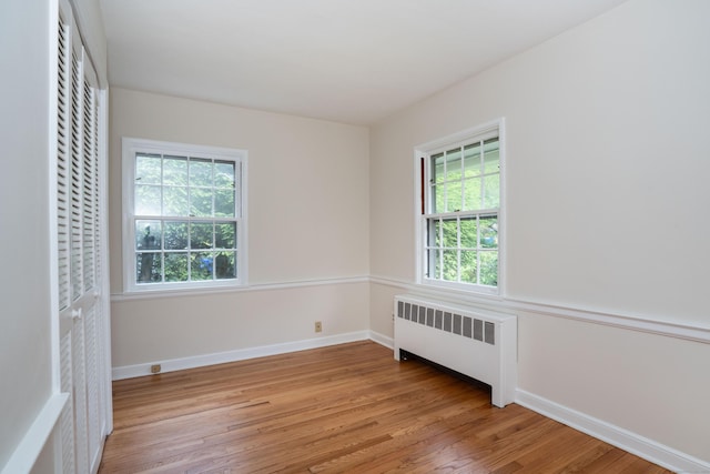 spare room featuring radiator heating unit, light wood-style floors, and baseboards