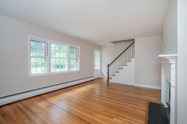 unfurnished living room with baseboard heating, light wood-style flooring, a brick fireplace, stairs, and baseboards