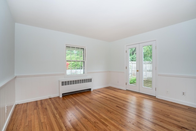 spare room featuring radiator heating unit, a wainscoted wall, wood-type flooring, and french doors