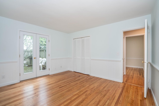 empty room featuring french doors, light wood-type flooring, and a wainscoted wall