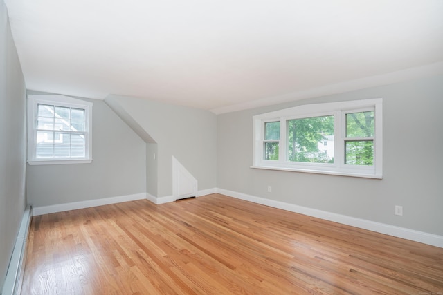 additional living space featuring a baseboard radiator, light wood finished floors, baseboards, and lofted ceiling