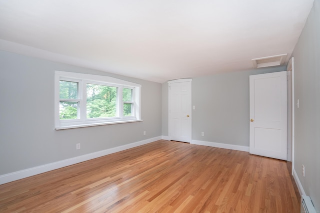 empty room featuring a baseboard heating unit, light wood-style floors, attic access, and baseboards