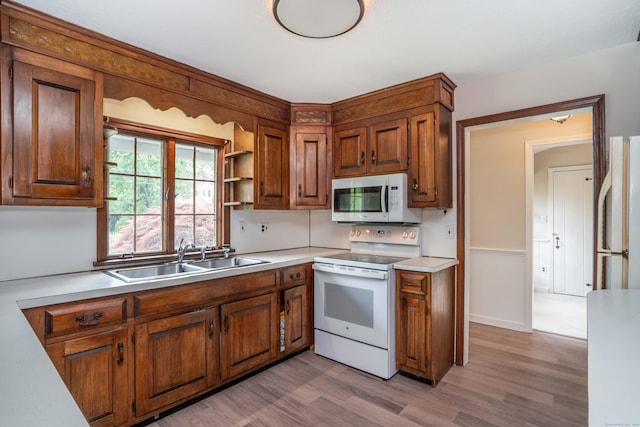 kitchen featuring white appliances, a sink, wood finished floors, brown cabinetry, and light countertops