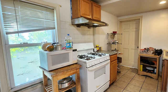 75 Clifton St, West Haven, CT 06516 - kitchen with white appliances, under cabinet range hood, light tile patterned floors, backsplash, and brown cabinetry