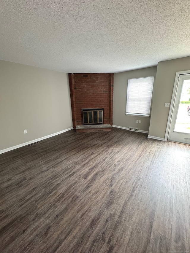 222 W Main St Apt 1C, Southington, CT 06479 - unfurnished living room with dark wood-style flooring, a textured ceiling, a brick fireplace, and baseboards