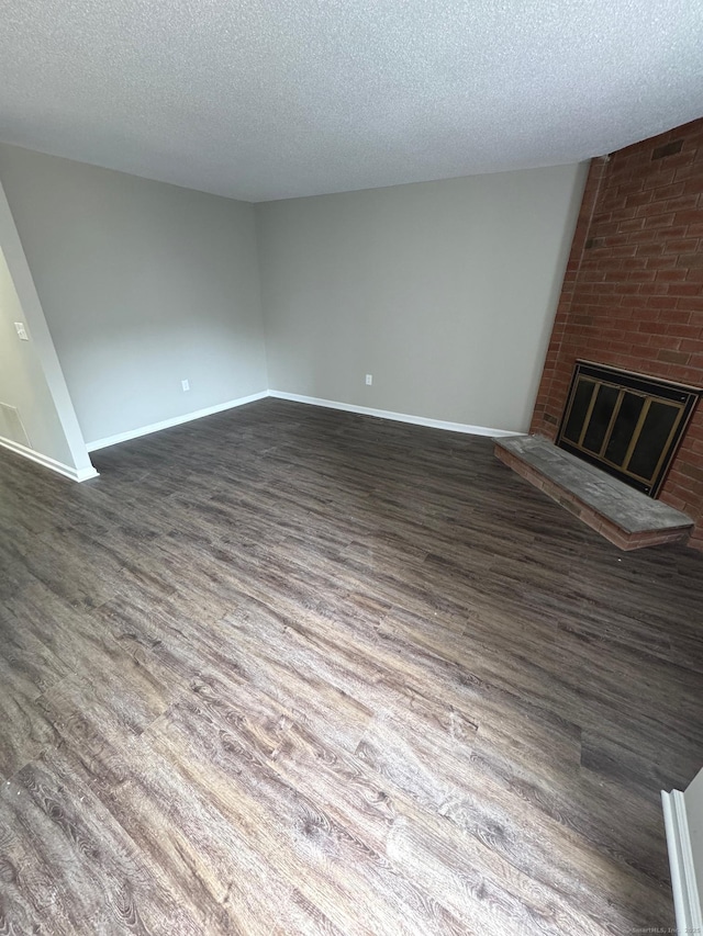 222 W Main St Apt 1C, Southington, CT 06479 - unfurnished living room featuring a textured ceiling, dark wood-style flooring, a brick fireplace, and baseboards