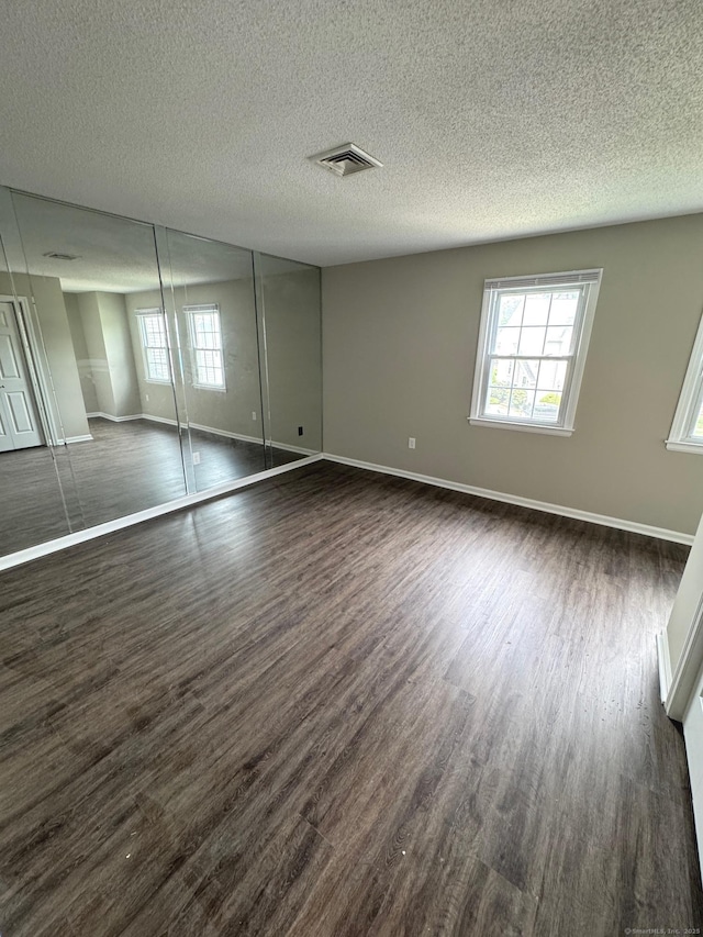 222 W Main St Apt 1C, Southington, CT 06479 - unfurnished bedroom with multiple windows, dark wood finished floors, baseboards, and a textured ceiling