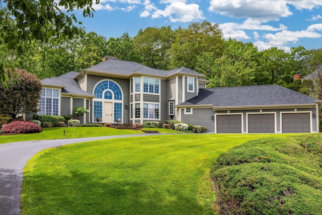 view of front facade featuring a front lawn, a chimney, asphalt driveway, and an attached garage
