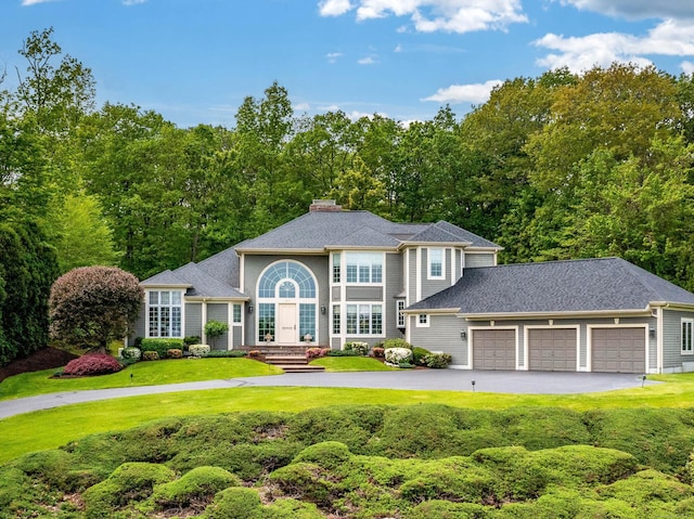 view of front of home featuring a front yard, asphalt driveway, a chimney, and a garage